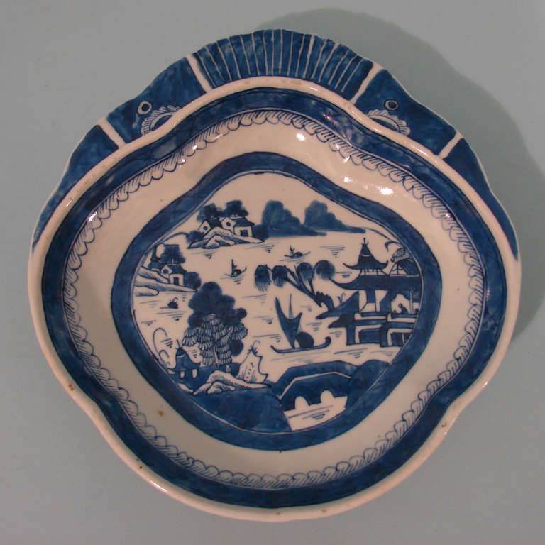 A Chinese Canton blue and white shrimp dish typically decorated overall with buildings and bridges, the irregular shaped dish with a fin motif at the top.
