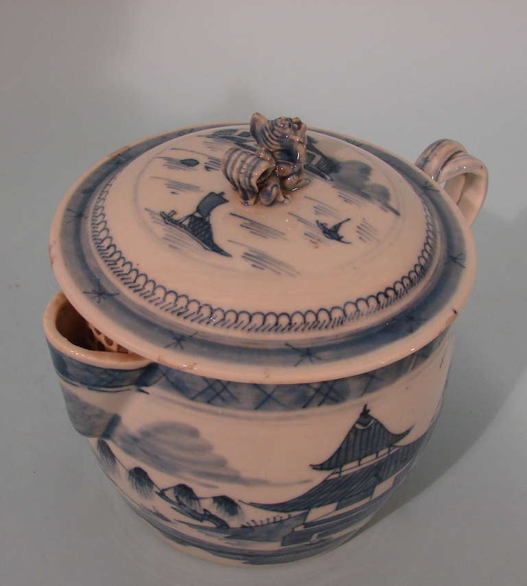 A Chinese Canton blue and white covered cider jug, the lid with a foo dog finial, the handle of intertwined form, decorated overall with river scenes and buildings. Circa 1860.