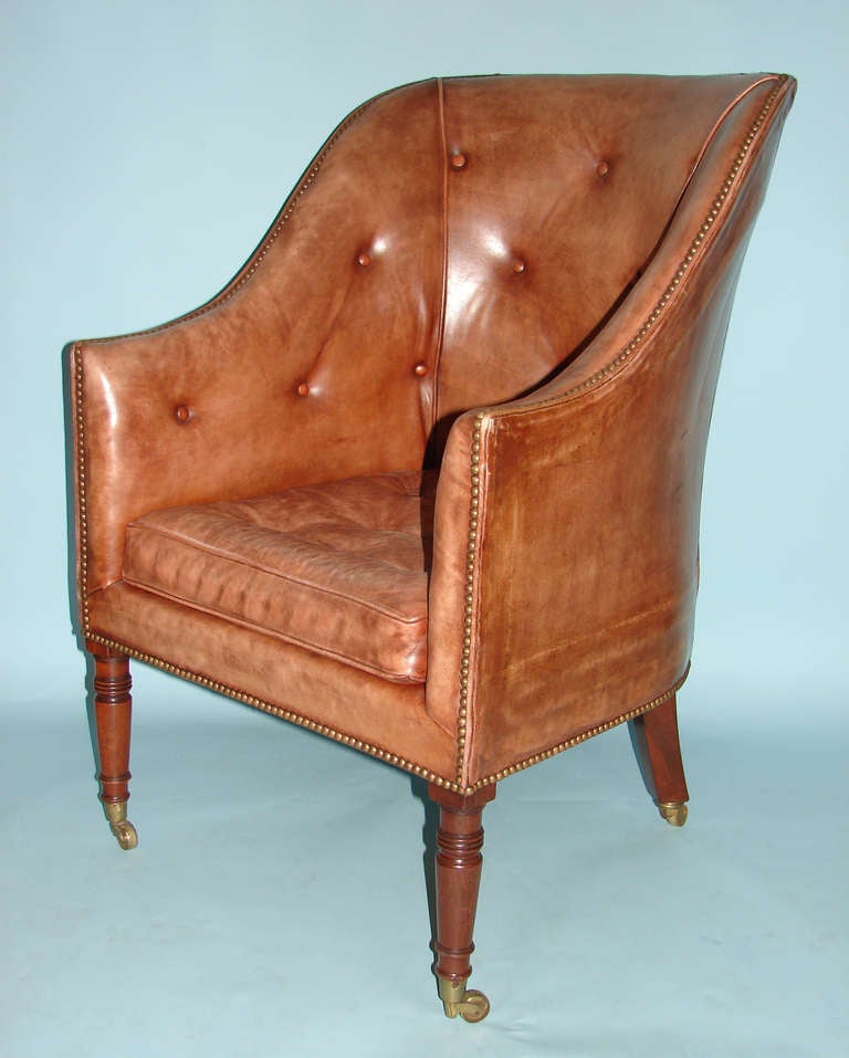 A late George III leather upholstered mahogany library chair, the curved back with downswept arms, all supported on ring-turned legs ending in casters.  Circa 1830.
