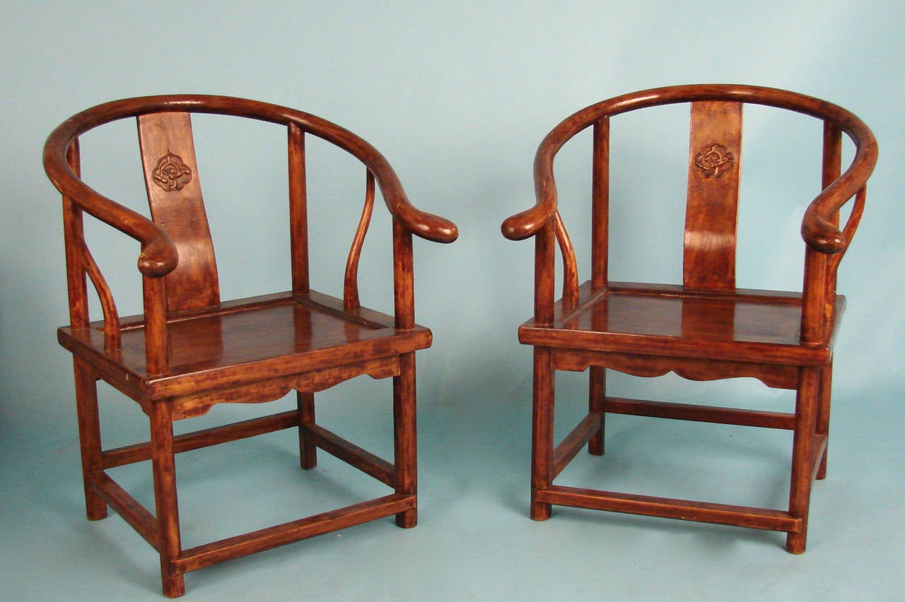 A pair of Chinese hardwood horseshoe back children's chairs, each with a carved back splat, supported on straight legs joined by stretchers.