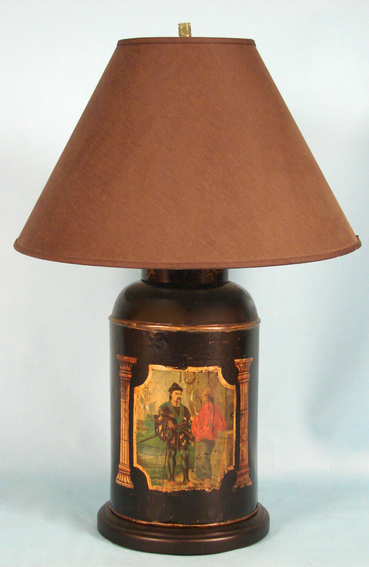 A Chinese export black and gilt decorated tole tea canister depicting two courtly gentlemen flanked by columns, the opposite side with stylized Chinese characters, now mounted with a wooden base and electrified for use as a lamp, circa 1880.