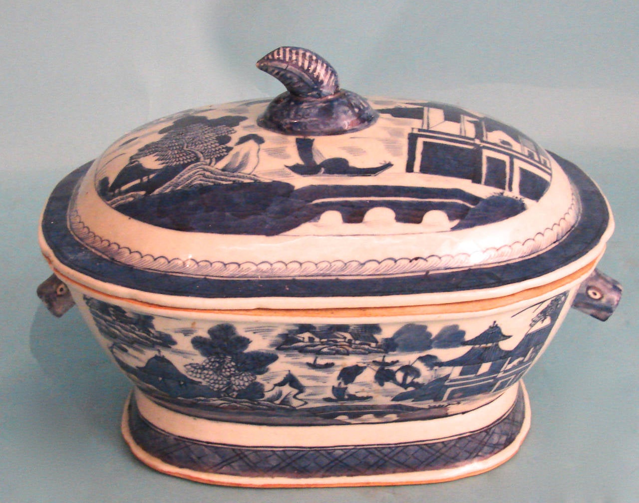 A Chinese export canton blue and white soup tureen with cover, the body with boar's head handles, the top with a stem finial, decorated overall in typical fashion with buildings in a river and mountain setting, circa 1860.
