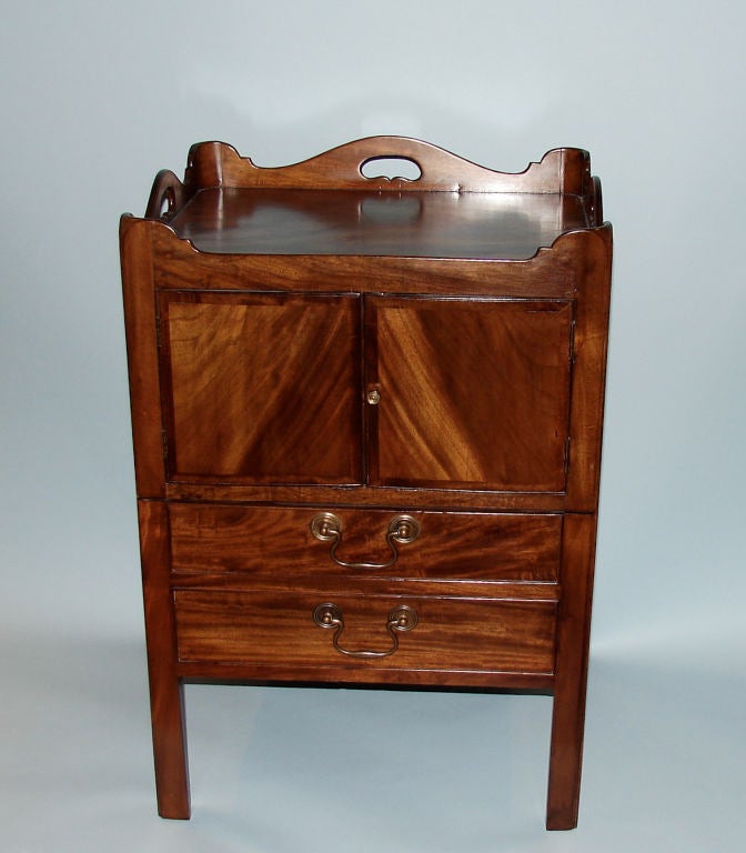 A George III figured mahogany bedside cabinet, the shaped top over2 cupboard doors above a deep drawer with bale handles. Circa 1790.
