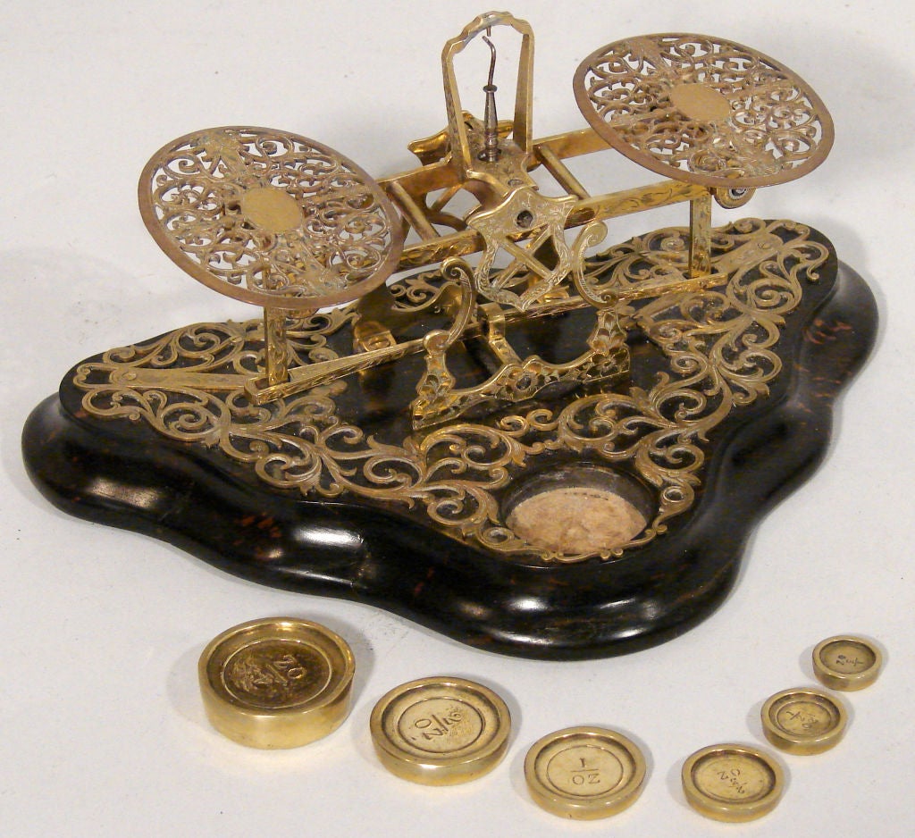 A highly decorative  English cut and engraved brass postal scale on a rosewood base made and signed by S. Mordan and Co. retaining its original complete set of 6 graduated weights. Circa 1880.