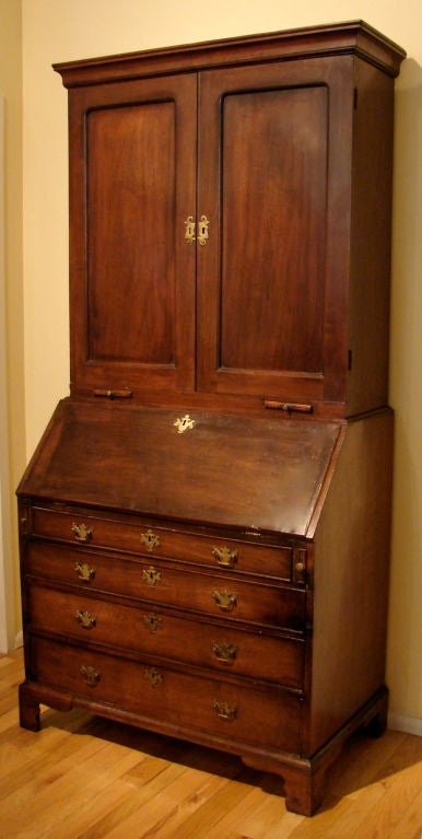 A George II red walnut slant front bureau cabinet, the top fitted with adjustable shelves and drawers, the interior of the lower stage with multiple drawers and a prospect door above four graduated drawers ending in bracket feet.  Circa 1750.