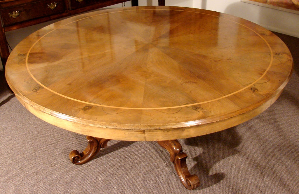 An Italian walnut center table, the line inlaid top with radial veneers over a columnar base terminating in four legs with upturned feet. Adjustable for use at 28 or 30 inches in height.