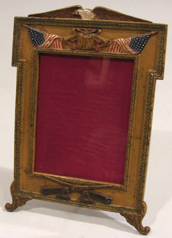 An unusual highly decorative American cast iron frame topped by a bald eagle with outstretched wings over a drum, bugles and flags, the crossed cannons representing the insignia of United States Field Artillery, the whole raised on short floral