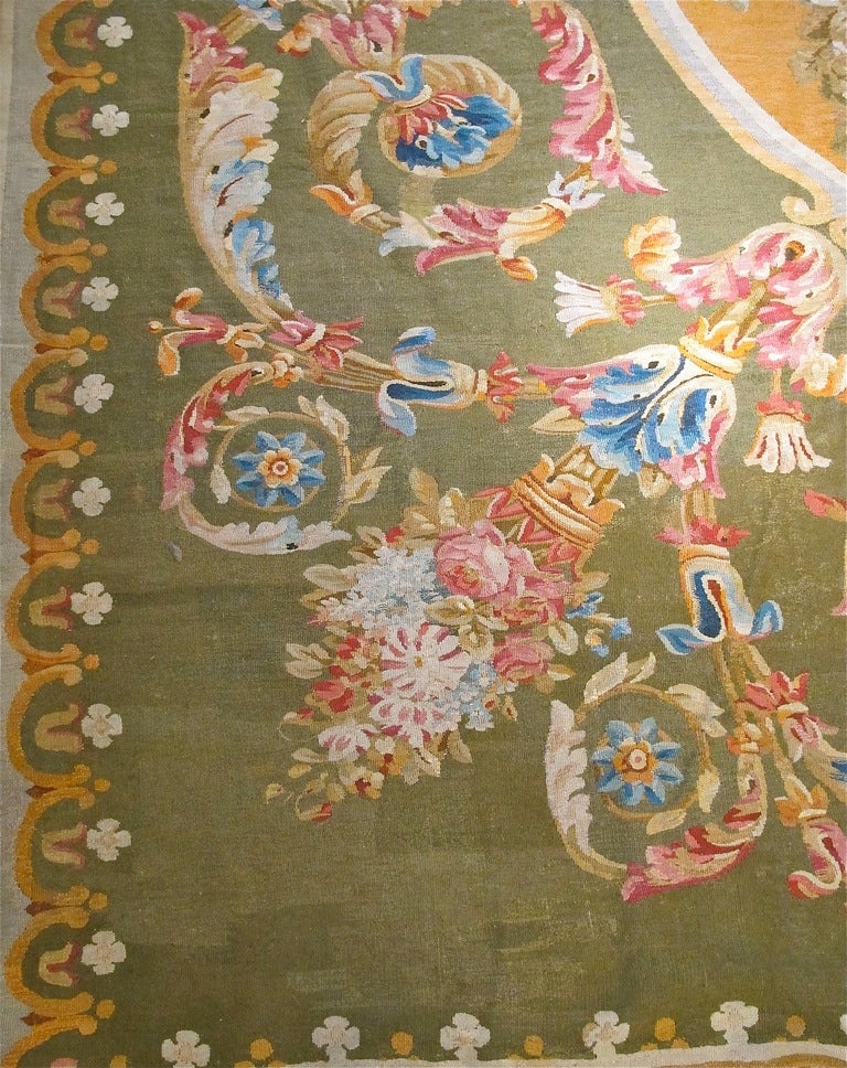 A grand and nearly square Aubusson carpet with a persimmon-gold oval medallion on a rich green background. The multicolored scrolling acanthus leaves with large lilies and other flowers brings a beautiful sense of movement to this design.