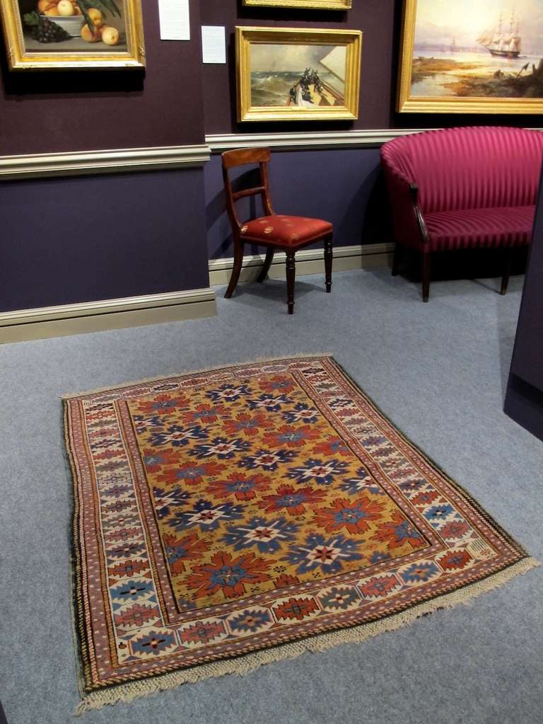 This charming Kuba rug from the South Caucasus is a very happy representation of Fine weaving from the region in the 19th century. Eight-pointed star-like blossoms are drawn rotating diagonally by color across a golden yellow ground. Depth is