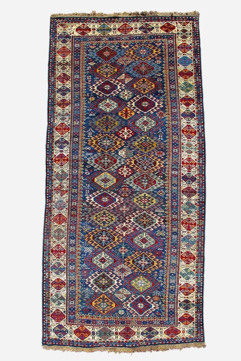 This Kuba long rug balances vivid color and a bold latch-hook pattern with fine detailing and attention to individual motifs. The two columns of latch-hook ornament are spaced so that a secondary column is formed from negative space. These