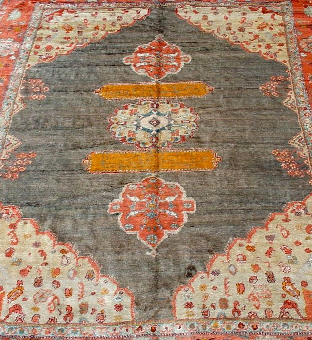 A soft, lush thick-piled carpet woven with central Anatolian angora wool. The small central medallion flanked by calligraphic cartouches and pendentives rests on a charcoal field. Persianate palmettes and vegetal devices are drawn within the bold