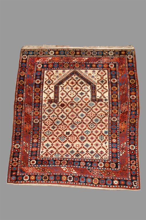 This antique Shirvan prayer rug from the South Caucasus combines a Classic white ground with a rare field pattern of a series of geometric motifs ranging from stars to quatrefoils within a lattice. This pattern continues within the inside of the