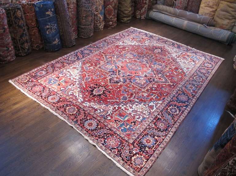 This classic Heriz carpet draws an elegant medallion against a madder-red ground. Tones of rose and brick are accented with indigo blues as white is used sparingly as a highlight, particularly within the corner-pieces. The meandering border is