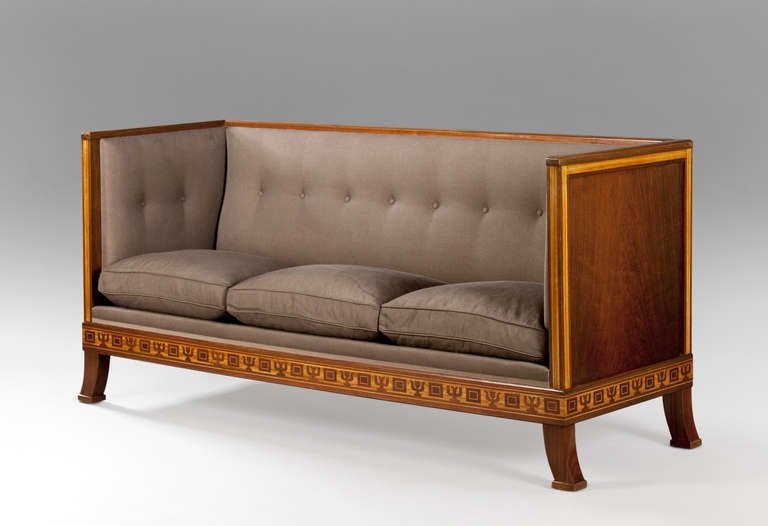 The rectilinear molded top-rail, above the conforming paneled and upholstered sides and back, the rectangular upholstered seat above a stylized marquetry frieze, on four saber legs.

Another suite with a sofa and two chairs of identical form