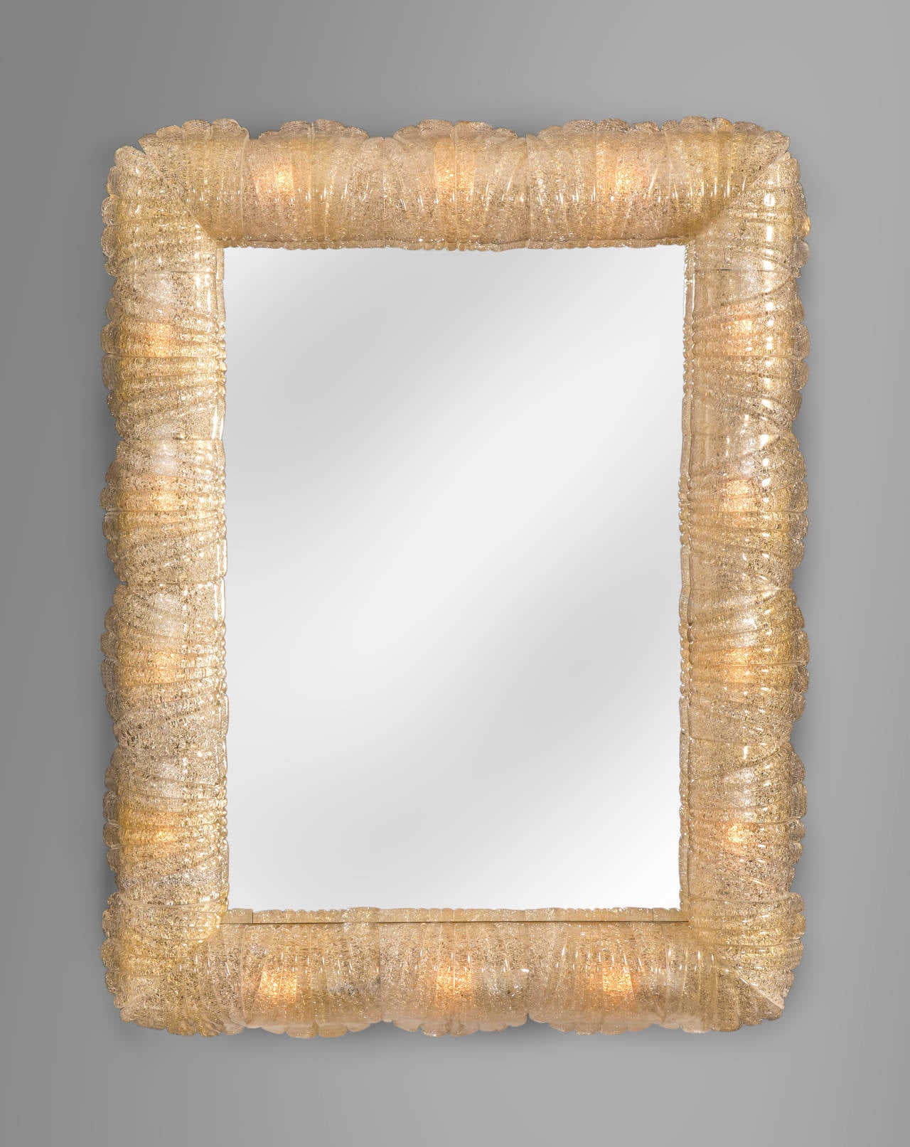 The magical Rugiadoso glass glows with a flattering light. The rectangular mirror plate inset in a brass border, within a frame composed of glass leaves with gold inclusions, softly illuminated by concealed lights.

One of two mirrors available.