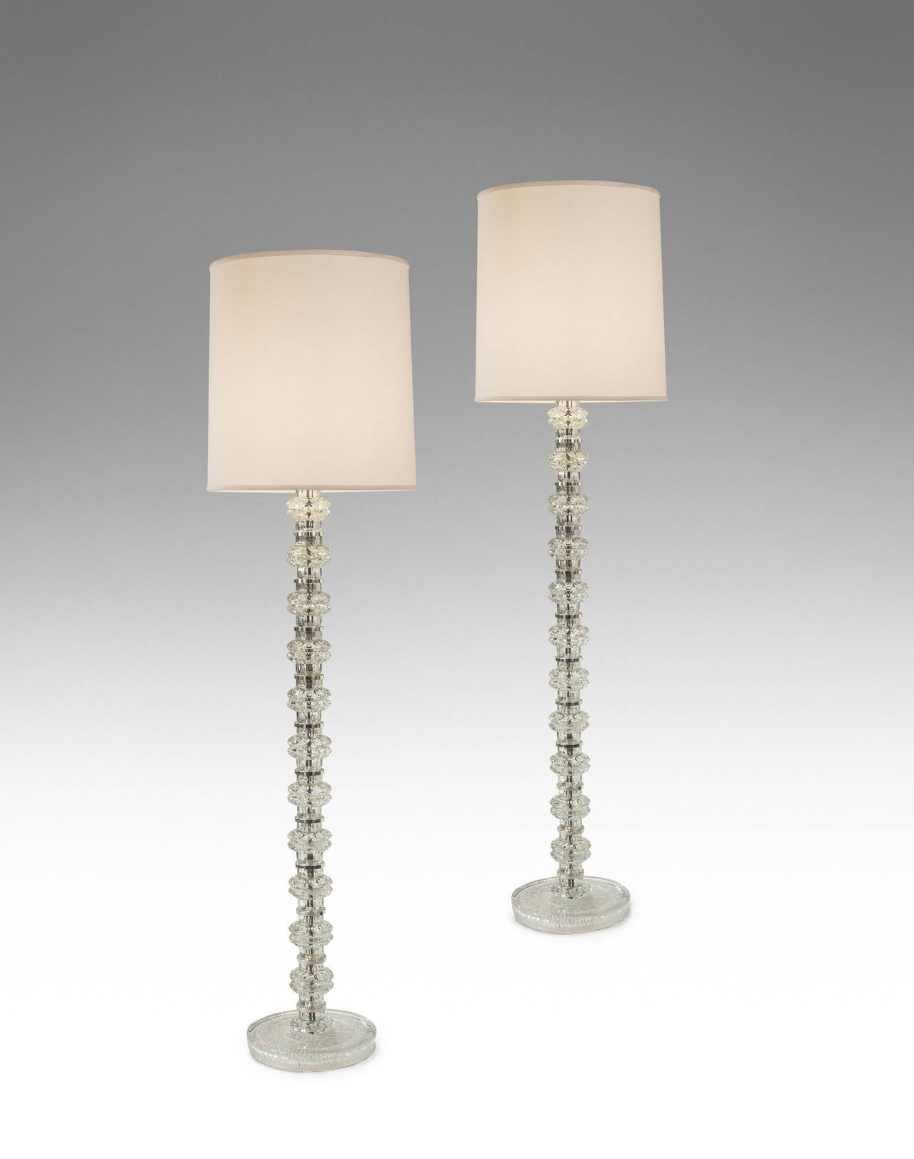 The delightfully complex, jewel like glass elements joined by silvered rings creating a remarkably powerful transparent standing lamp. Each standard composed of facetted glass sections, above a circular molded glass base, mid-20th century.