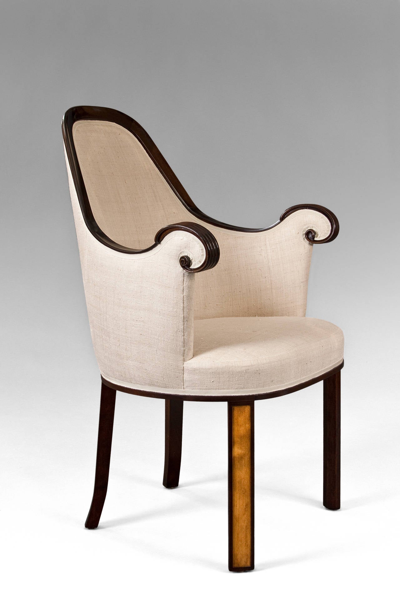 Crowned with a sinuous wooden arch rising above an upholstered back, terminating in reeded scrolled armrests, the rounded seat rests on paneled rectangular legs, with two brass manufacturer plaques: 