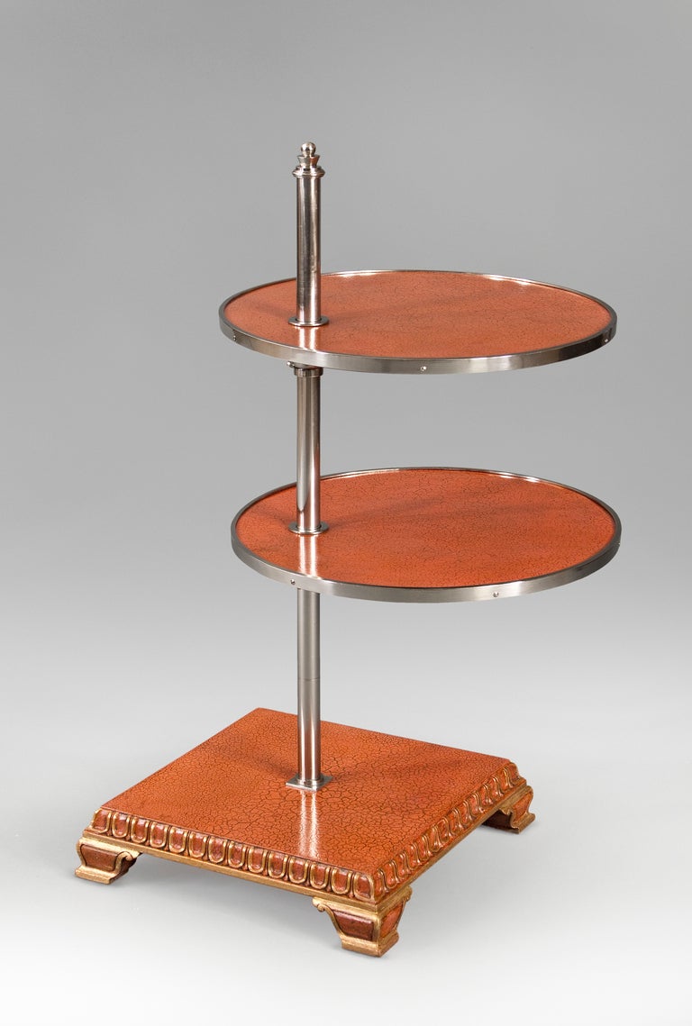 Description: The metal banded adjustable round shelves, supported by a central nickel cylinder surmounted by a stylized finial, above a square pedestal base with tongue and dart molding, on bracket feet. 

1 of 2 available

Examples of similar