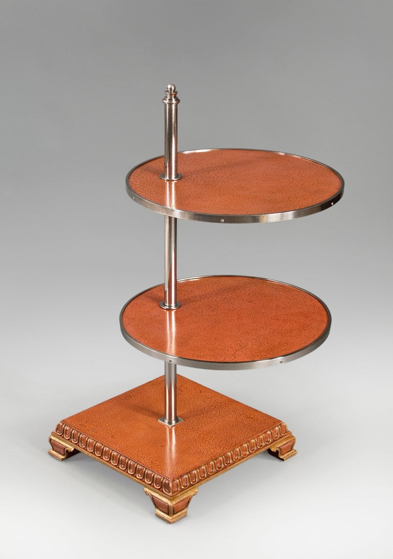The metal banded adjustable round shelves, supported by a central nickel cylinder surmounted by a stylized finial, above a square pedestal base with tongue and dart molding, on bracket feet. 

1 of 2 available

Examples of similar tables are