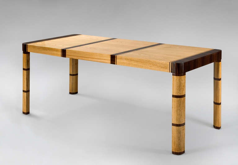 The rectangular table with rounded corners and inlaid with four traverse bands of macassar ebony, above a conforming freeze, on banded demilune legs, with 3 leaves of 21.5