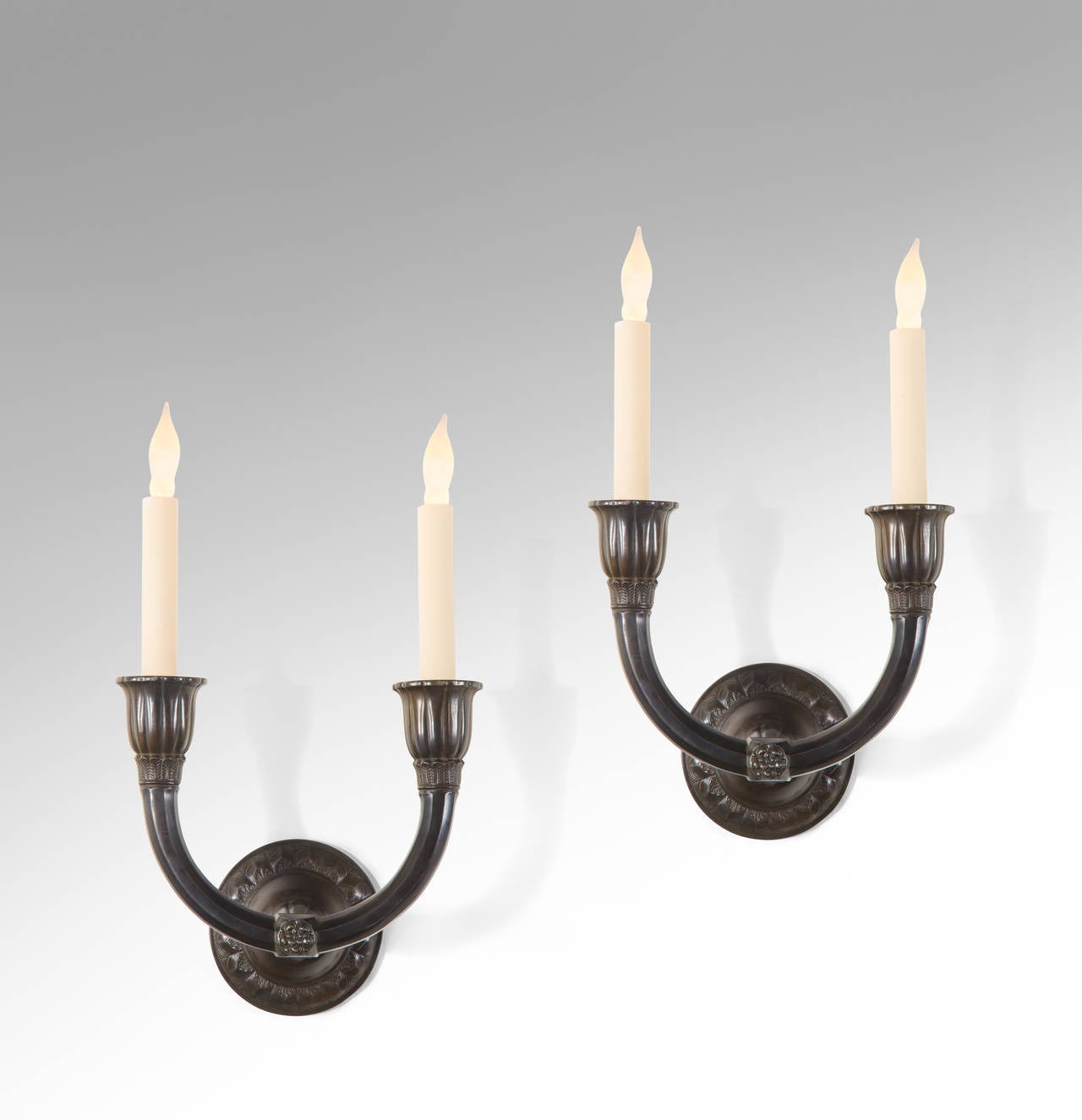 Each with an circular backplate with incised foliate pattern, issuing a center post with paired trumpet shaped light holders.