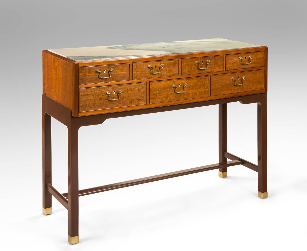 The dramatic green and white marble top, inset in a rectangular frame, above seven molded drawers each centering a keyhole and brass pull, on an umber lacquered stand with an H-shaped stretcher and brass feet

A related cabinet is illustrated by