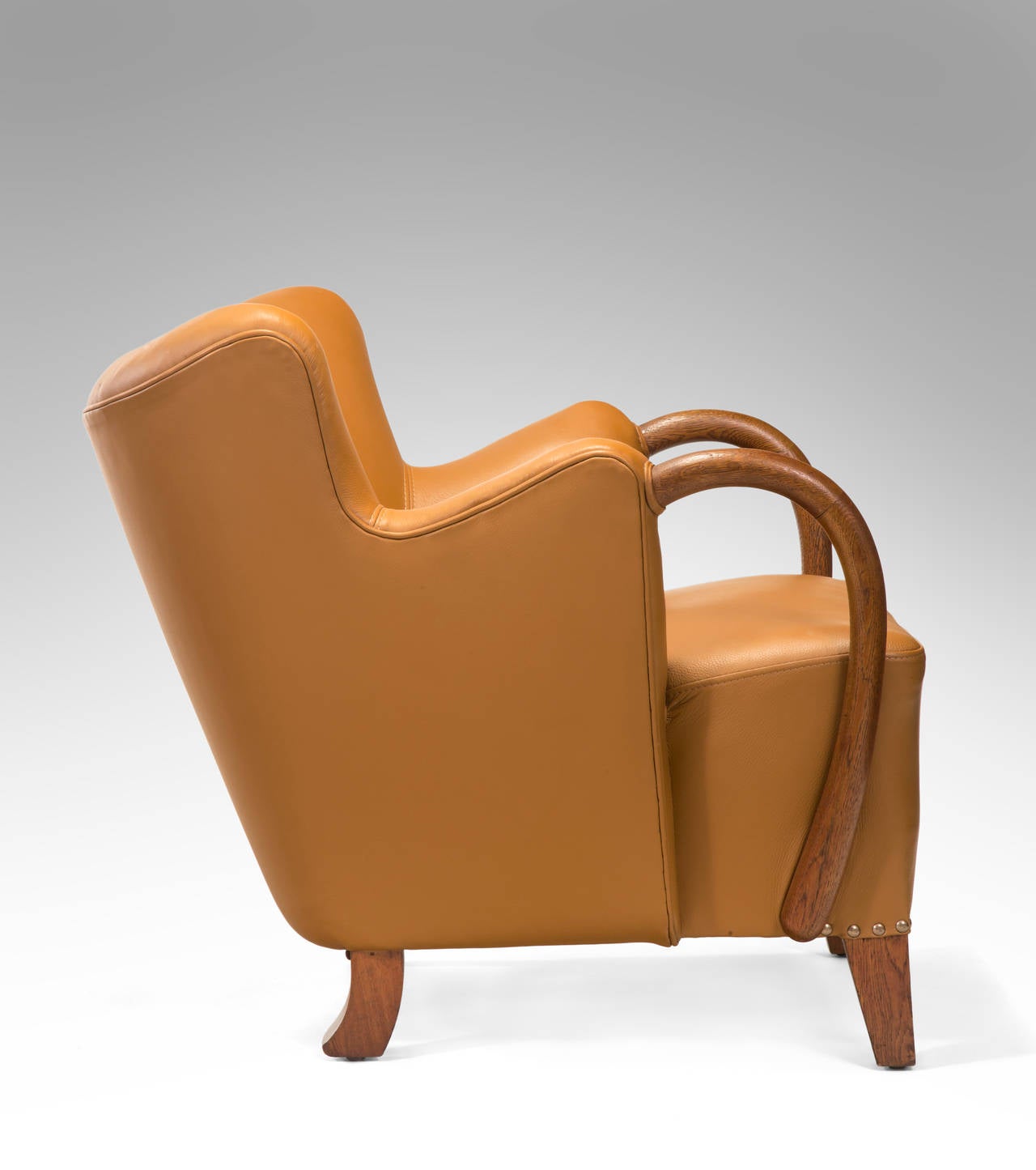 Curvaceous, exuberant, and superbly made in limited production, this chair perfectly capture the essence of 1940s Danish design.  The curved backrest, issuing pronounced arching wooden armrests, above a rectangular seat, terminating in square front