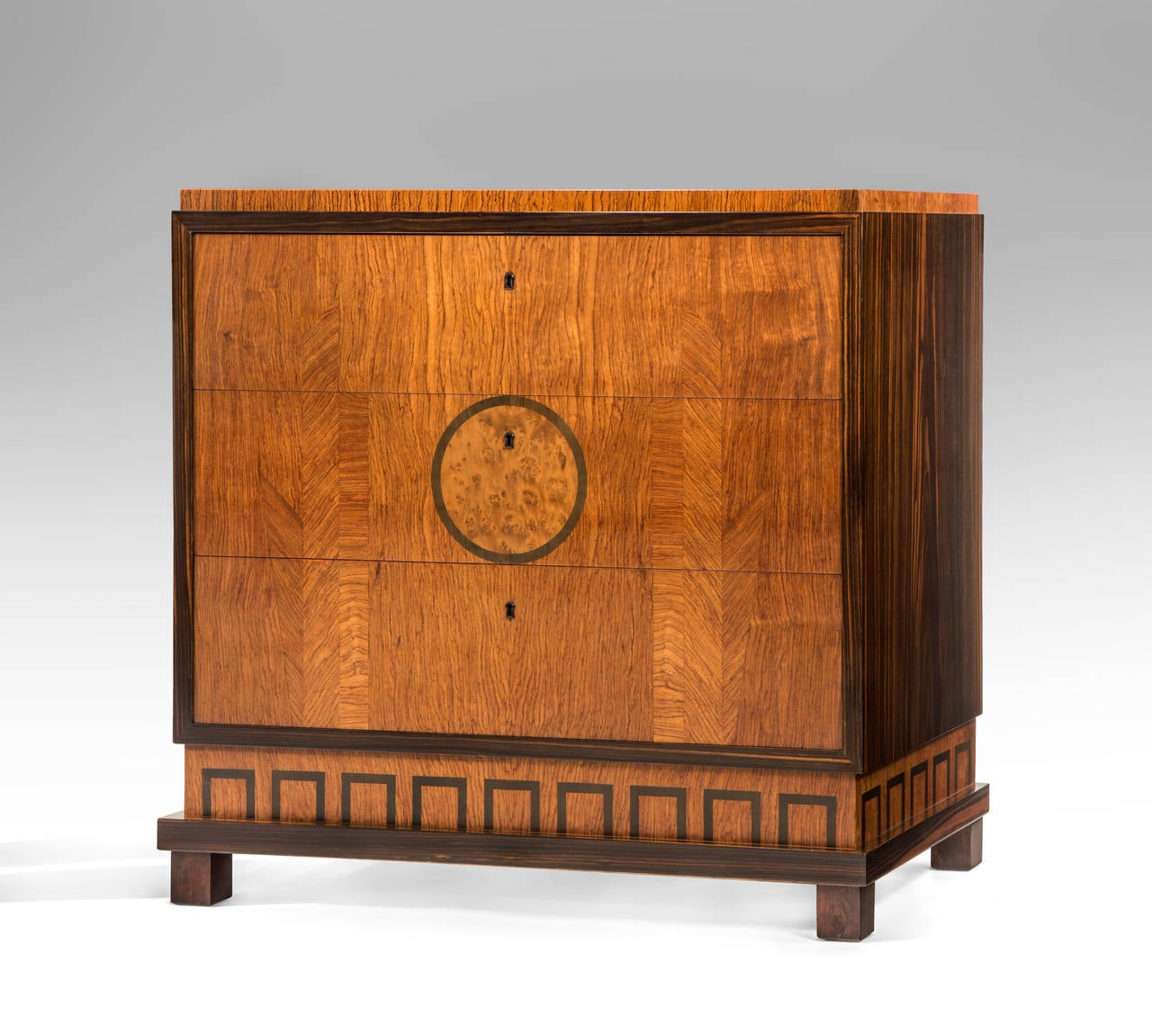 The rectangular top above 3 drawers framed by a macassar border, the center drawer with circular burl-redwood medallion, above a fretwork pattern base, raised on square feet.