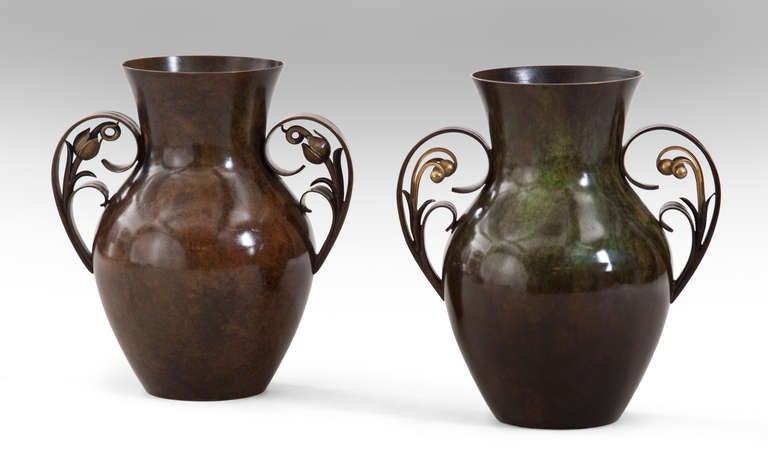 The pair of urn-form vases with complementary bronze patinations, one vase issuing two unfurling leaf-like handles with spiral stamen, the other vase issuing two unfurling leaf-like handles each with three polished bronze berries.  One marked:
