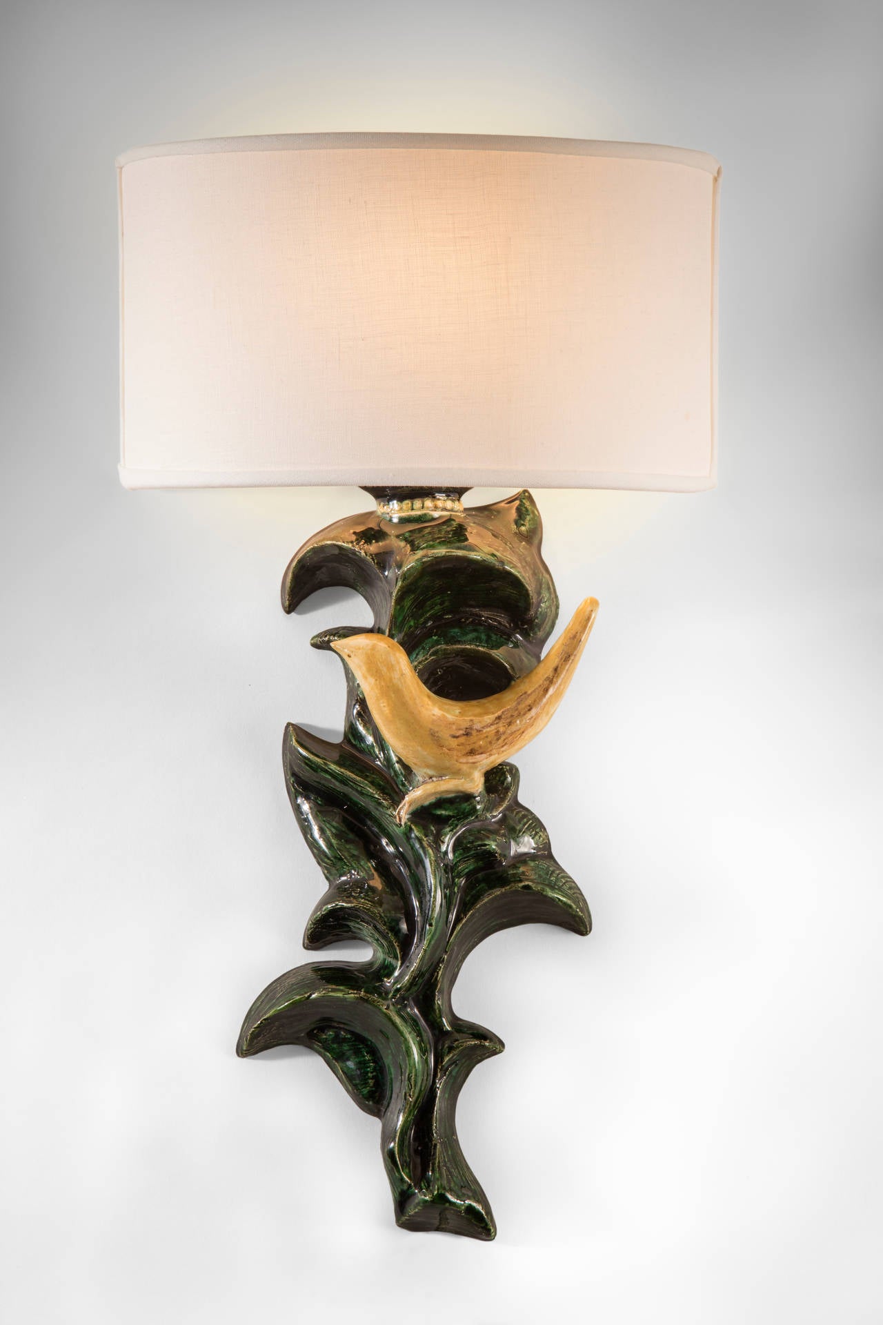 Stylish and charming, the golden bird perched on cascading, lustrous green leaves. Each richly glazed faience standard depicting a stylized songbird perched amongst scrolling branches, surmounted by a beaded cup bobeche and curved shade, signed PVP,