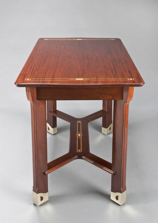 The rectangular top with slightly convex sides, rounded corners and a molded edge, adorned in stylized inlay, on four rectangular legs with curving capitals and canted corners, connected by a linear stretcher, terminating in pierced brass feet. <br