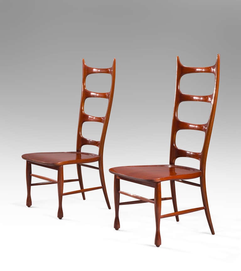 The beautifully carved high back chairs have a sophisticated sculptural quality. The back composed of four lozenge shaped cross braces joined to the curved and pointed uprights, the shaped seat above legs joined by stretchers.

Provenance: Casa