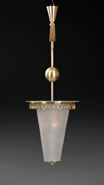 The conical corona, above a tasseled cord and brass globe, centering a circular glass over a looped brass apron, the conical reticello filigrana glass shade terminating in a circular finial. <br />
<br />
This piece @ H.M. Luther Antiques<br