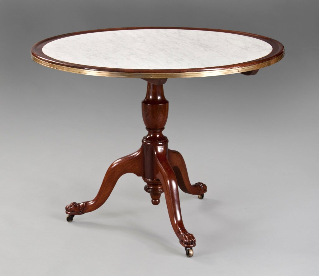 The circular white marble top within a mahogany frame bound by brass molding, above a balustrade stem, on three curved legs terminating in paw feet on casters. 

More tables available at: www.hmluther.com

This piece @ H.M. Luther