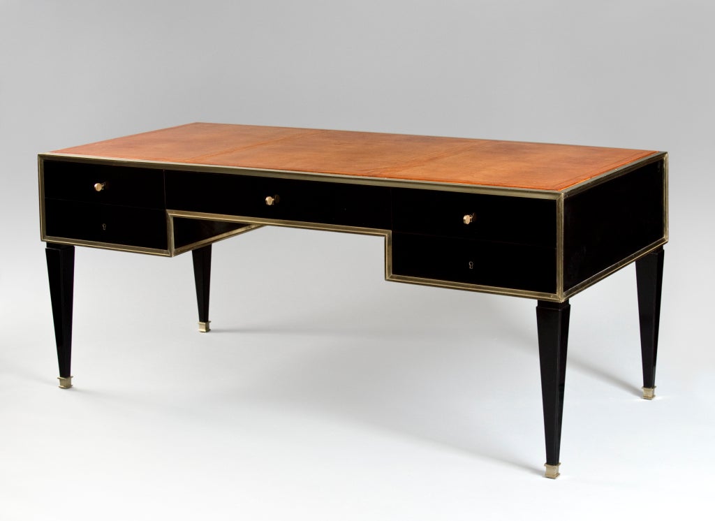 The rectangular gilt-tooled inset patinated leather writing surface, above four drawers centering a kneehole below an additional drawer, banded throughout in cast brass molding, raised on square tapering legs, terminating in sabots.

Marc du