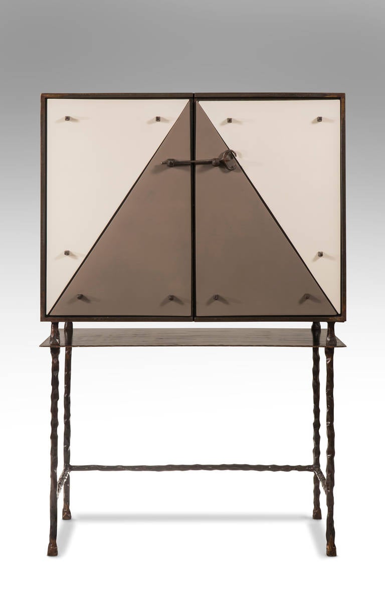 The rectangular top, above a conforming cabinet fronted by two gray and white terracotta inset metal doors, each door adorned in decorative fasteners and secured by a sculpted iron pin, the interior with an adjustable shelf and built-in openings for