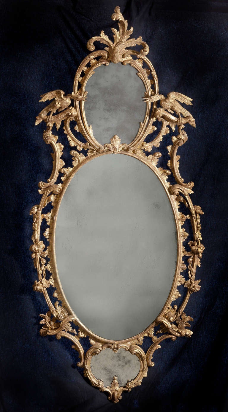 A fine three-plate rococo oval mirror, crested by an oval surmounted with an acanthus spray, flanked by rocaille, with ho-ho birds perched on foliated c and s-scrolls that flank a large central plate, the central plate rests atop a smaller oval