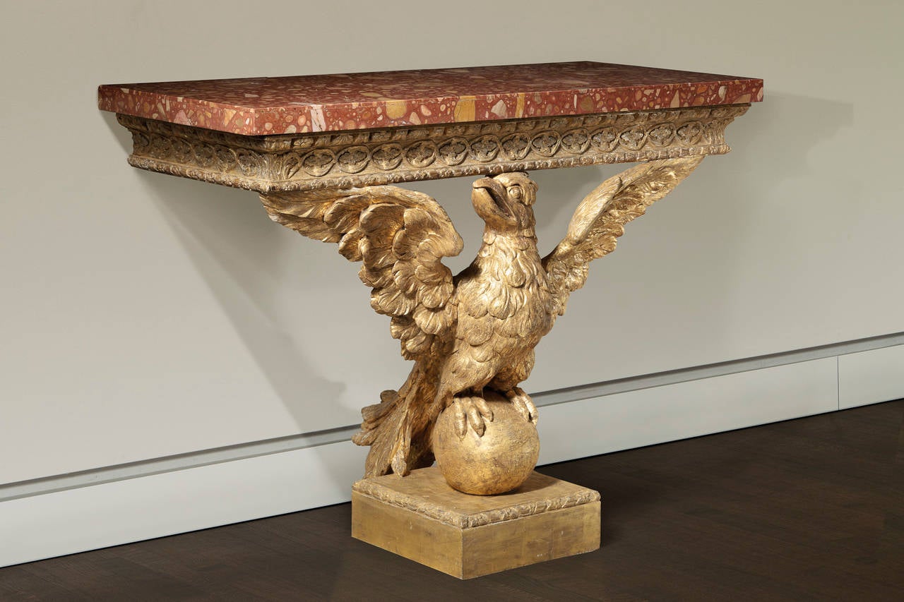 A pair of console tables in the manner of William Kent with marble tops supported by a carved and gilded frieze having egg, shell, and flower carving with quatrefoil carvings in intertwined oval scrolls over a ribbon and rosette moulding supported
