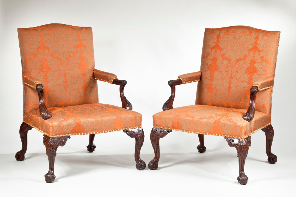 An important pair of George III carved mahogany armchairs, in the manner of Paul Saunders, with upholstered serpentine shaped backs and seats, the arms on downswept supports with carved C-scrolls and acanthus decoration, raised on fluted cabriole