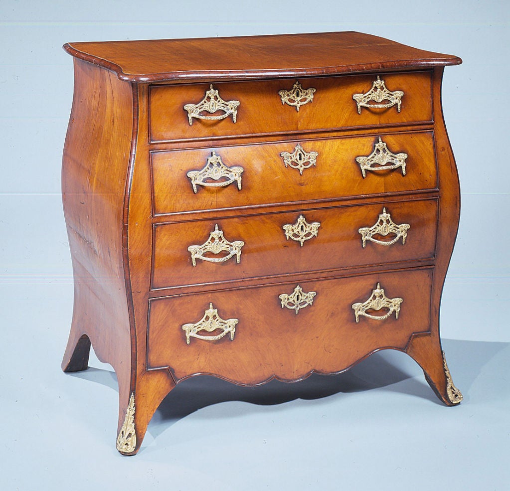 A small padauk wood bombe shaped commode with very good color, having a serpentine top and original gilt brass handles and enrichments, beaded drawers and a shaped base with beading.