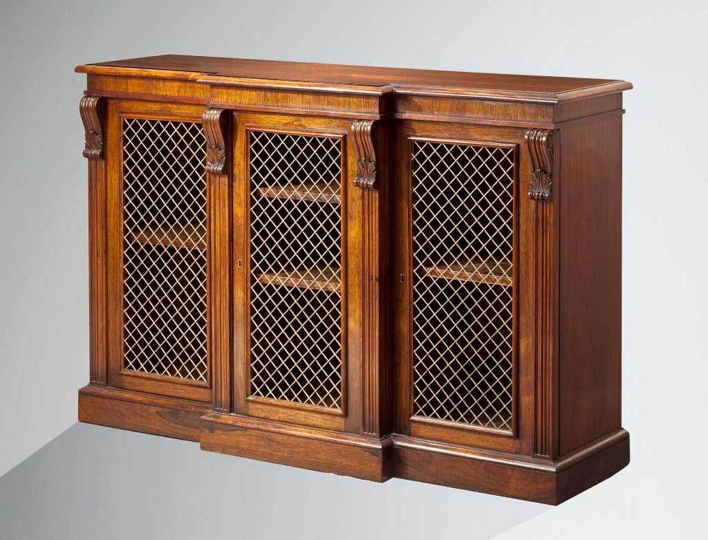 A fine small rosewood breakfront cabinet in the manner of Gillows having a molded top with a plain frieze over three brass grill doors with molded columns flanking the doors headed with carved scrolls resting on a plinth base.