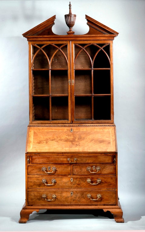 A superb George II bureau bookcase in the manner of Thomas Chippendale, of nicely faded mahogany having a straight broken neck pediment with dentil moulding centered by a stop fluted urn with entwined ribbon carving and a spiral fluted finial. 
The