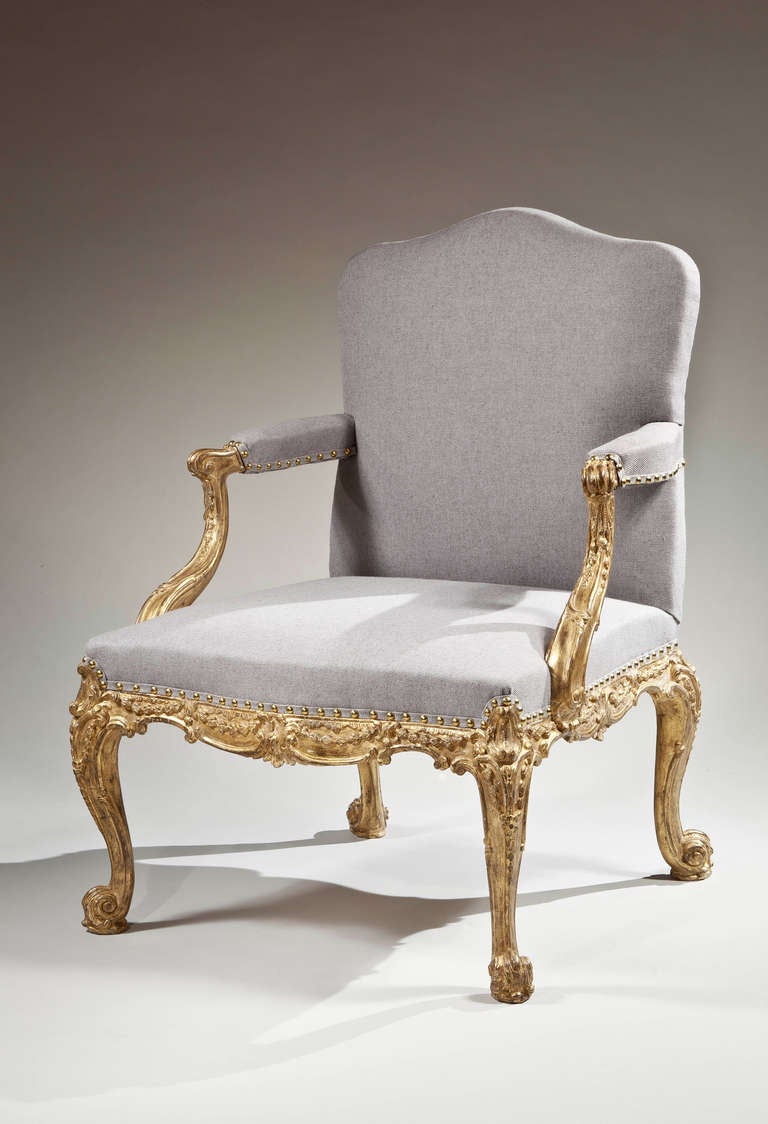 A finely carved and gilded open armchair having an upholstered seat and back and elbow rests with carved hand rests supported by double c-scroll arms with trailing bell flowers, the frame having a shaped apron of c-scrolls with trialing bell flowers