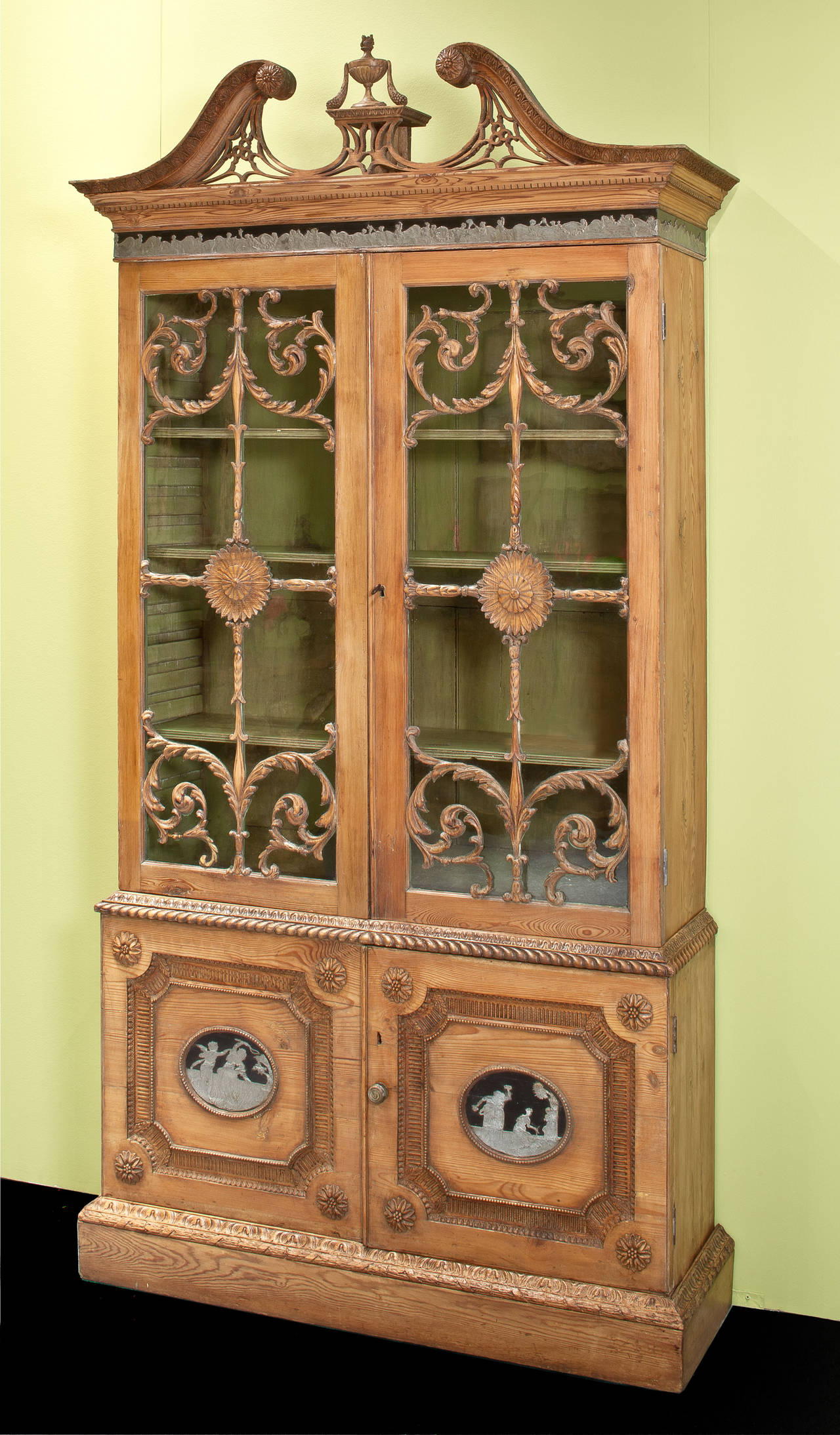 George III carved pine bookcase over cabinet, in the manner of Robert Adam, elaborately carved with pewter mounted ornaments depicting classical figures, likely originally painted.  English Circa 1775 				
The use of pewter on this bookcase relates