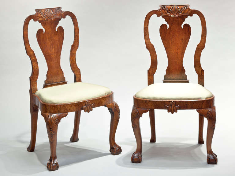 A pair of George II carved walnut side chairs in the manner of Giles Grendey, the moulded shaped top rails with shell and floral carving above vase-shaped splats flanked by shaped uprights with drop in saddle shaped seats, with carved shells in the