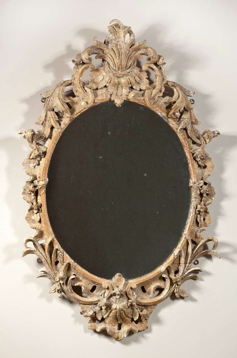 A fine carved and gilt oval rococo mirror crested with an acanthus leaf spray with carved and gilt foliage around the frame terminating in double c-scrolls flanking a cabochon with rocaille.  Originally oil gilt, dry stripped in restoration. 