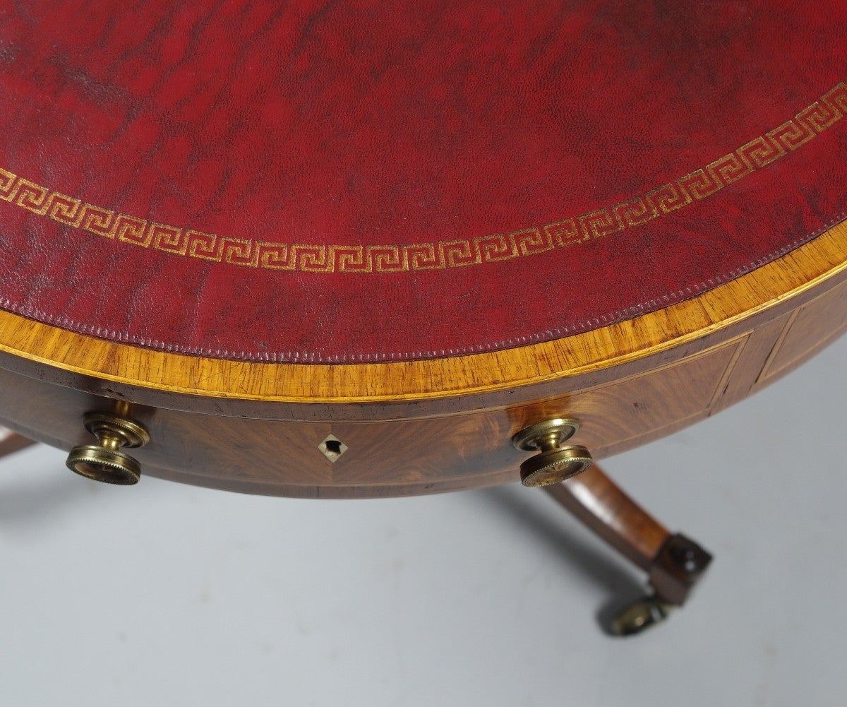 A diminutive drum table having an inset leather top banded in tulipwood and boxwood stringing, the drawer fronts having bookmatched veneers in Goncalo alves and banded in satinwood and ebony resting on a solid pillar of Goncalo alves, the tripod