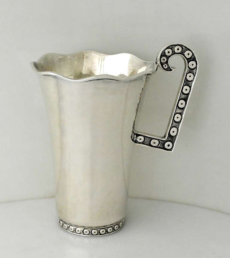 Being offered is a circa 1980s sterling silver pitcher by Tane of Mexico City. Modernist design with tapering body; D-shaped handle with circular oxidized pattern to handle and banded foot. Dimensions: 9