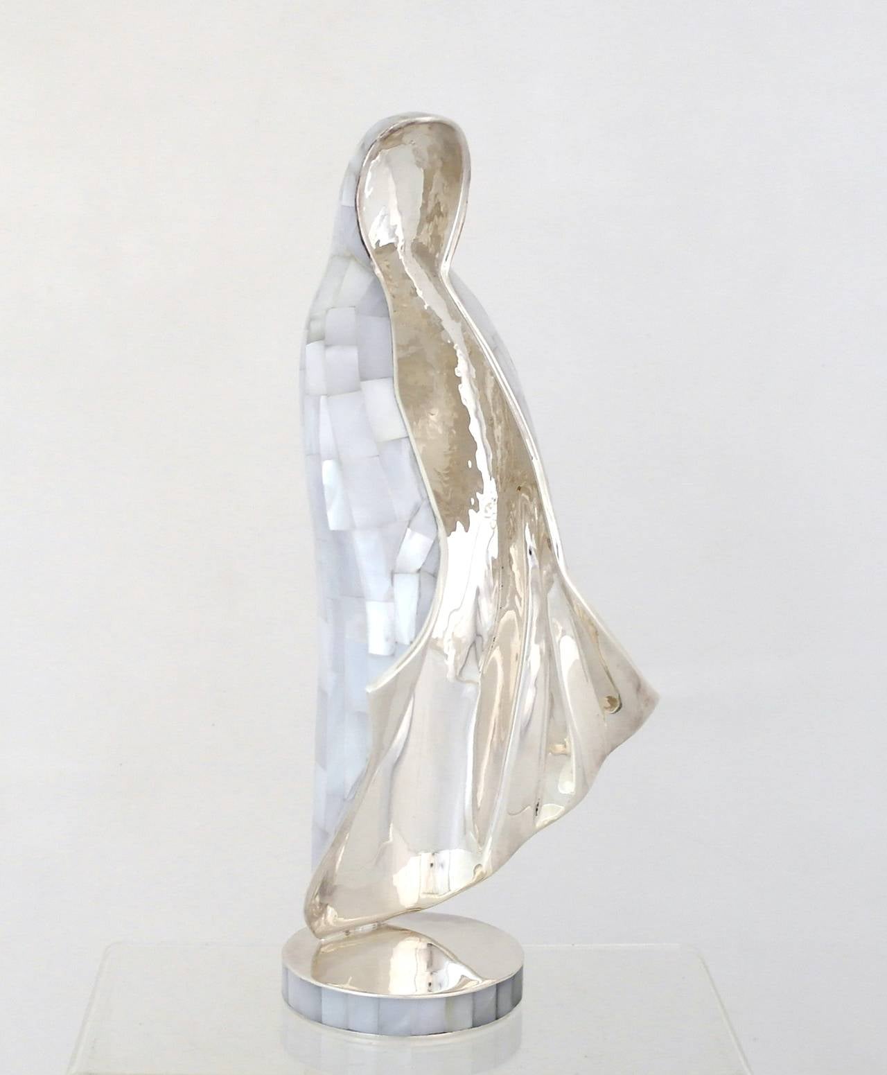 Being offered is a statue of Mother Mary by Los Castillo of Taxco, Mexico. Handmade object with mother of pearl inlay, standing on a circular base with similar mother of pearl inlay on rim of base.  The flowing design of this modernistic