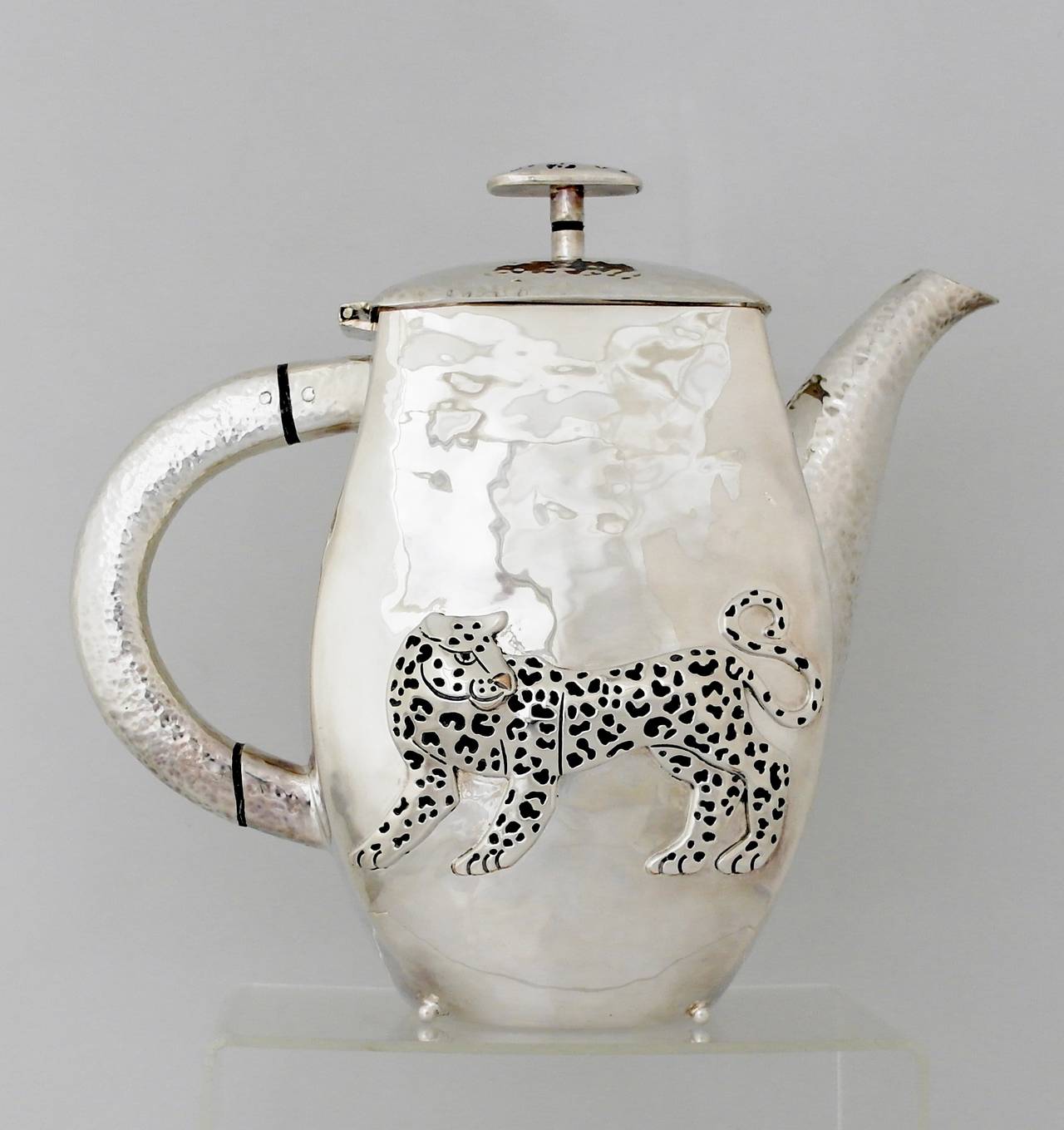 Being offered is a circa 1990 pitcher by Emilia Castillo of Taxco, Mexico. Hand-wrought piece with spot hammering throughout. Applied leopard on opposite sides of the body; matching striped finial. Dimensions: 10 inches height x 11 inches from